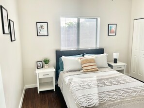 A bedroom with a bed, bedside tables, a window with blinds, and framed pictures on the wall. - Bright 1BR Retreat | Central Miami (Miami)