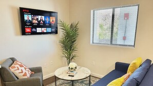 Un saló amb un sofà, un butacó, una taula de centre i una televisió que mostra Netflix.