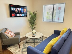 A living room with a sofa, armchair, coffee table, and a TV displaying Netflix. - Bright 1BR Retreat | Central Miami (Miami)