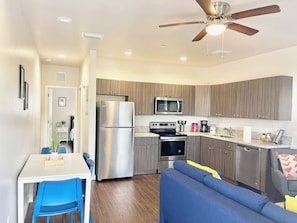 A compact kitchen with modern appliances, a dining area with blue chairs, and a ceiling fan. - Bright 1BR Retreat | Central Miami (Miami)