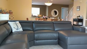 A sectional sofa with a decorative pillow, a dining table with chairs, a staircase, and a wall-mounted mirror. - Rehoboth 4BR Townhome Sleeps 10 Bike to Beach (Rehoboth Beach)