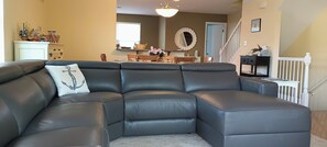 Ein modulares Sofa mit einem Zierkissen, ein Esstisch mit Stühlen, eine Treppe und ein wandmontierter Spiegel.
