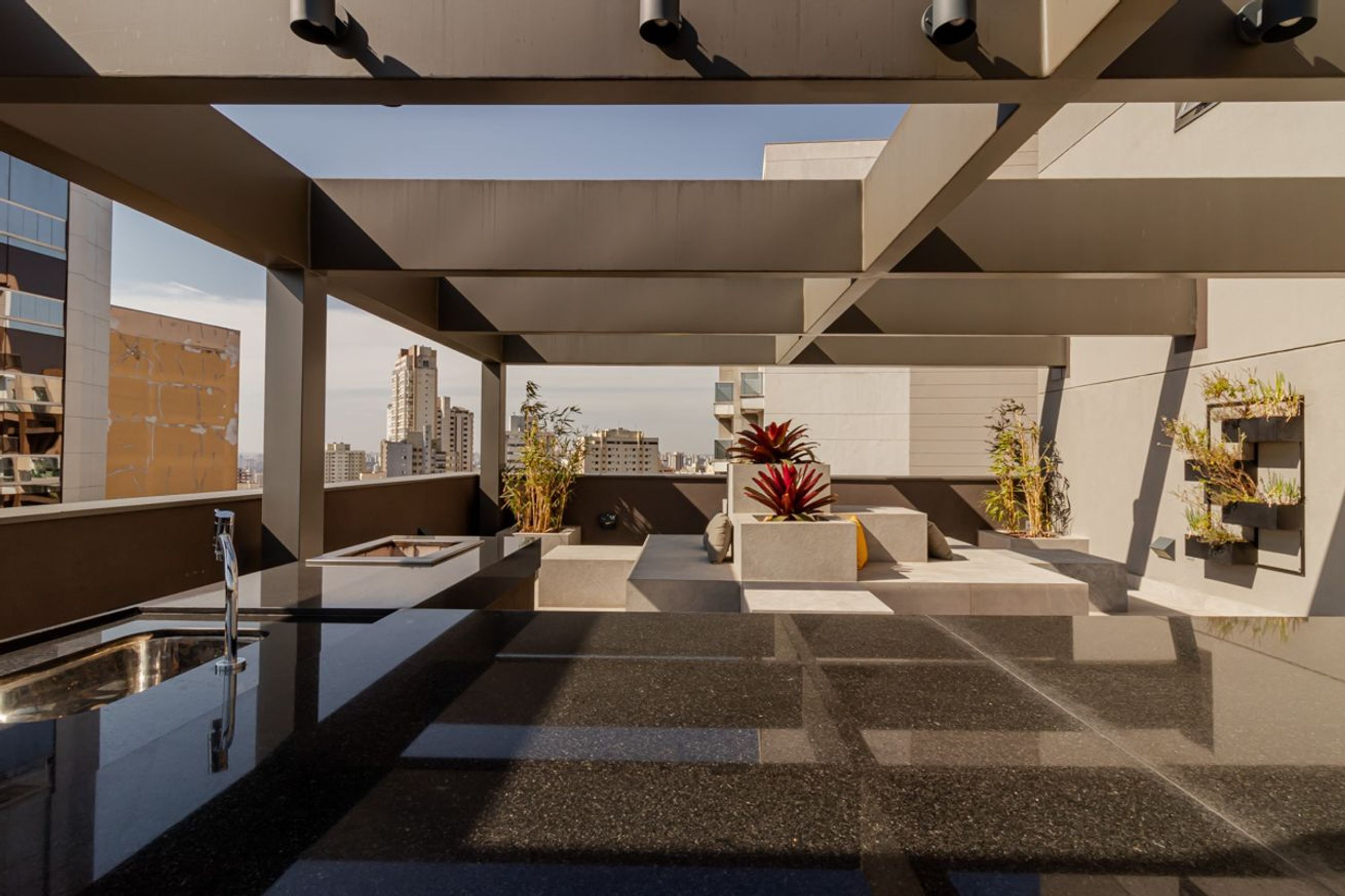 A rooftop terrace with a modern design, including a sink, potted plants, and a view of the city skyline.