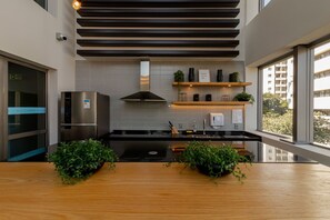 Eine moderne Küche mit einem Edelstahlkühlschrank, einem eingebauten Backofen, einer schwarzen Arbeitsplatte und Holzregalen mit Pflanzen.