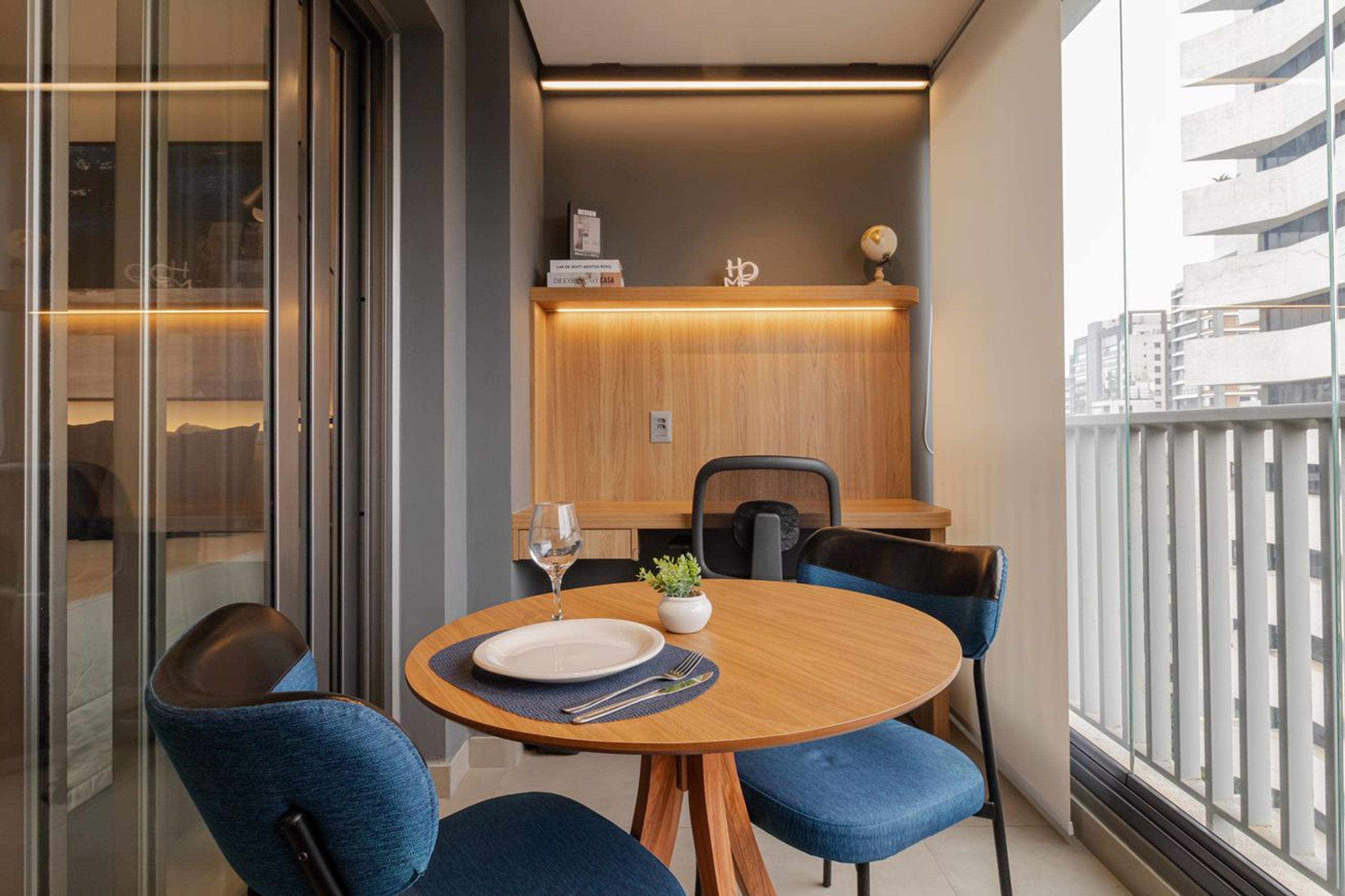 Un espace repas moderne avec une table ronde en bois, des chaises à revêtement bleu, une petite plante en pot et un verre à vin.