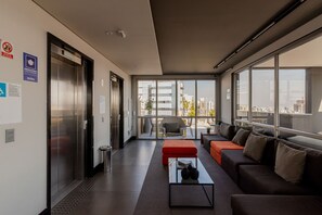 Eine moderne Hotelhalle mit Aufzug, Sitzgelegenheiten und großen Fenstern mit Blick auf die Stadt.