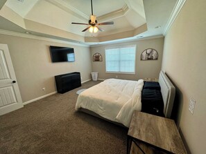 A bedroom with a bed, a ceiling fan, a TV, a window with blinds, and a wall-mounted artwork.