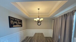 A dining room with a wooden table, white paneled walls, a chandelier, and a sign reading 'GAME ROOM'. - Spacious Family Home• Sleeps 8 • Near Ft Campbell (Clarksville)