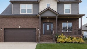 A two-story house with a garage, a front porch, and a well-maintained lawn. - Spacious Family Home• Sleeps 8 • Near Ft Campbell (Clarksville)