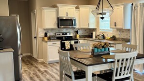 A kitchen with white cabinets, a microwave, a stove, and a dining table with chairs. - Spacious Family Home• Sleeps 8 • Near Ft Campbell (Clarksville)