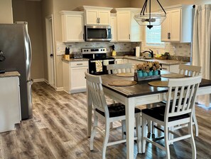 Una cocina con armarios blancos, microondas, estufa y una mesa de comedor con sillas.