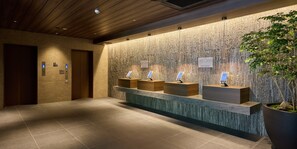 A reception area with a wooden ceiling, a reception desk with multiple counters, and a large potted plant.