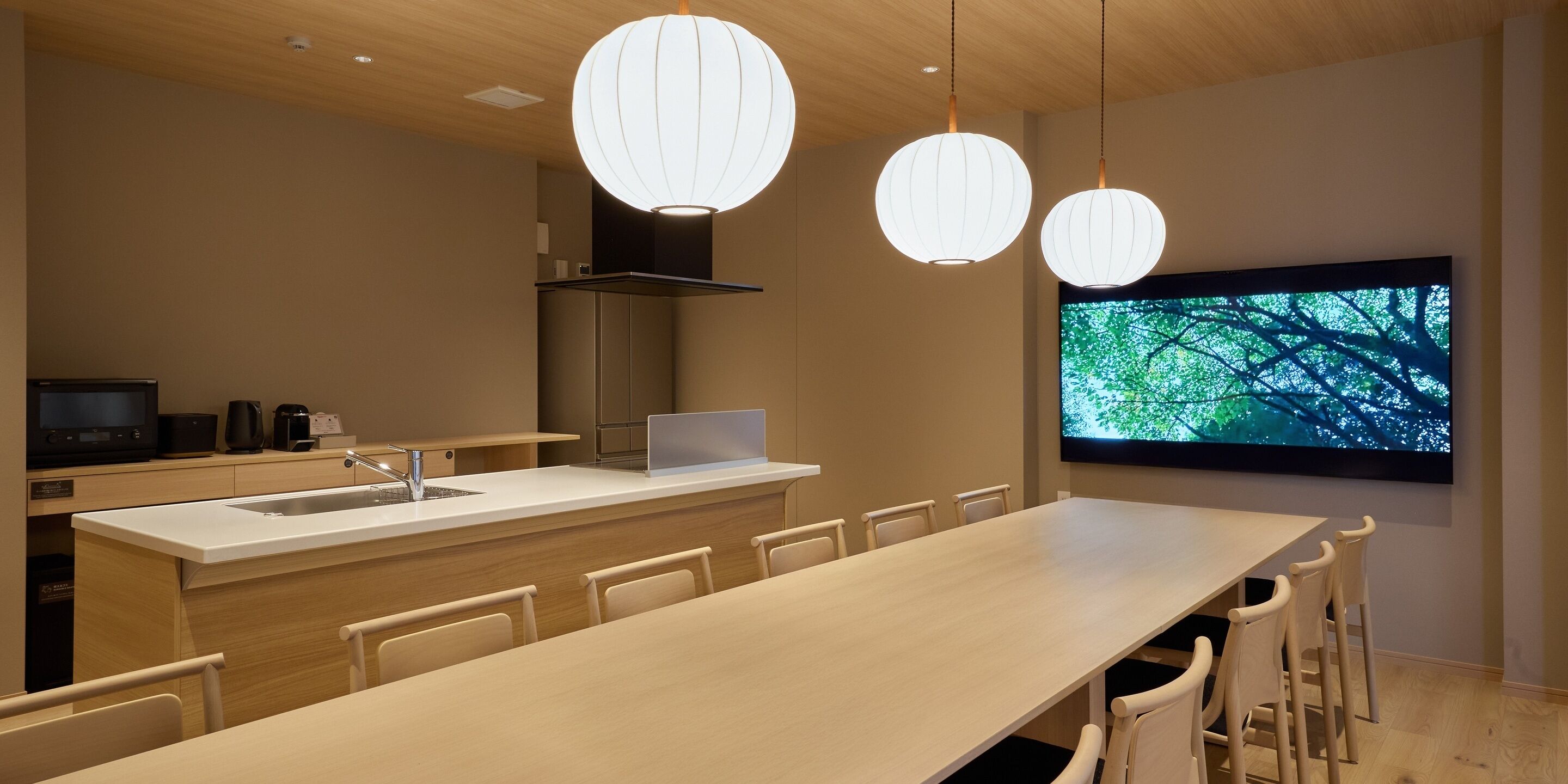 A modern kitchen with a central island, a dining area with chairs, and a large TV screen displaying a nature scene.