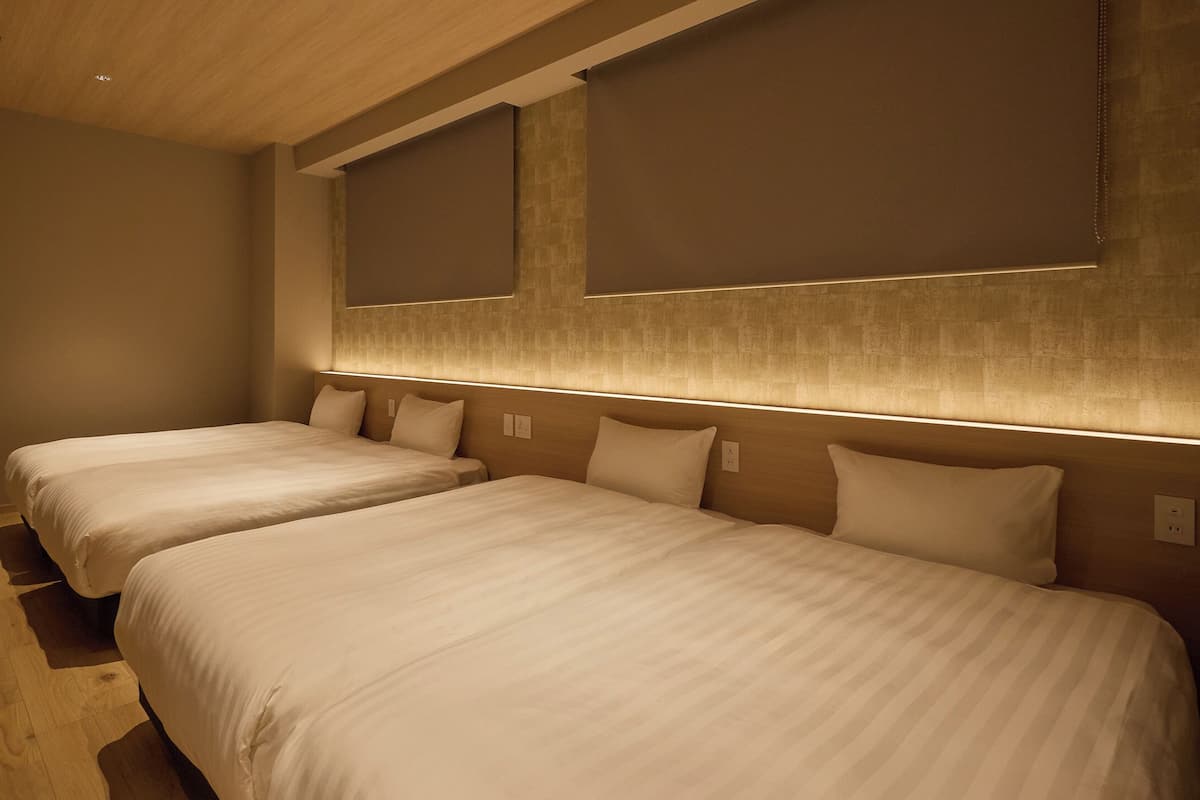 A hotel room with two beds, wooden flooring, and a modern design.