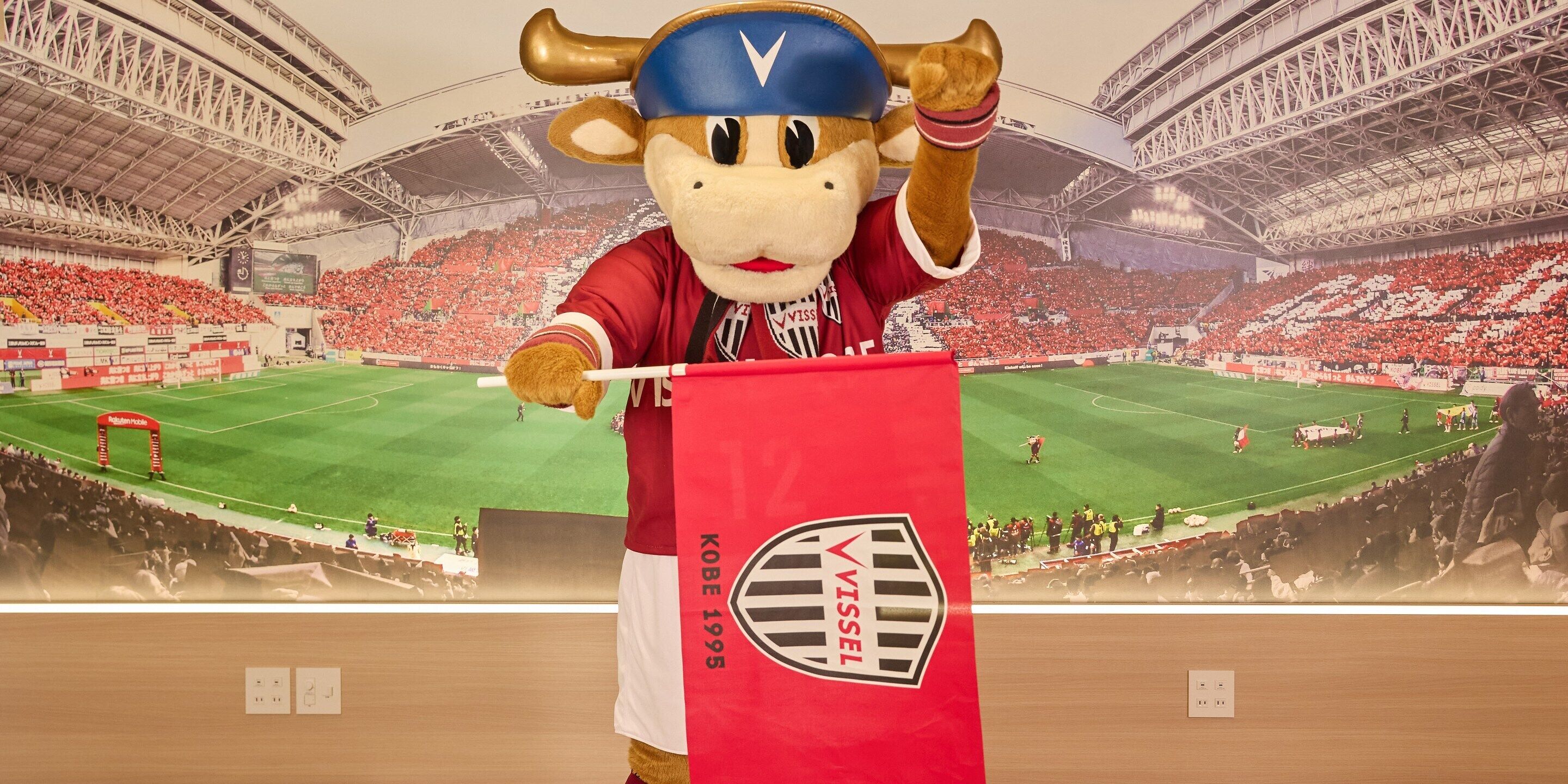 A mascot in a stadium with a large red banner.