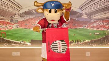 A mascot in a stadium with a large red banner.