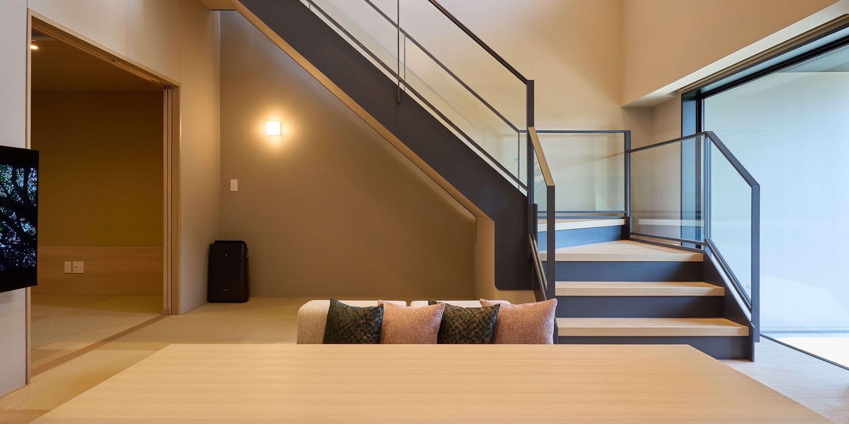 Un interior moderno con una escalera, un televisor de pantalla plana y un sofá con cojines.