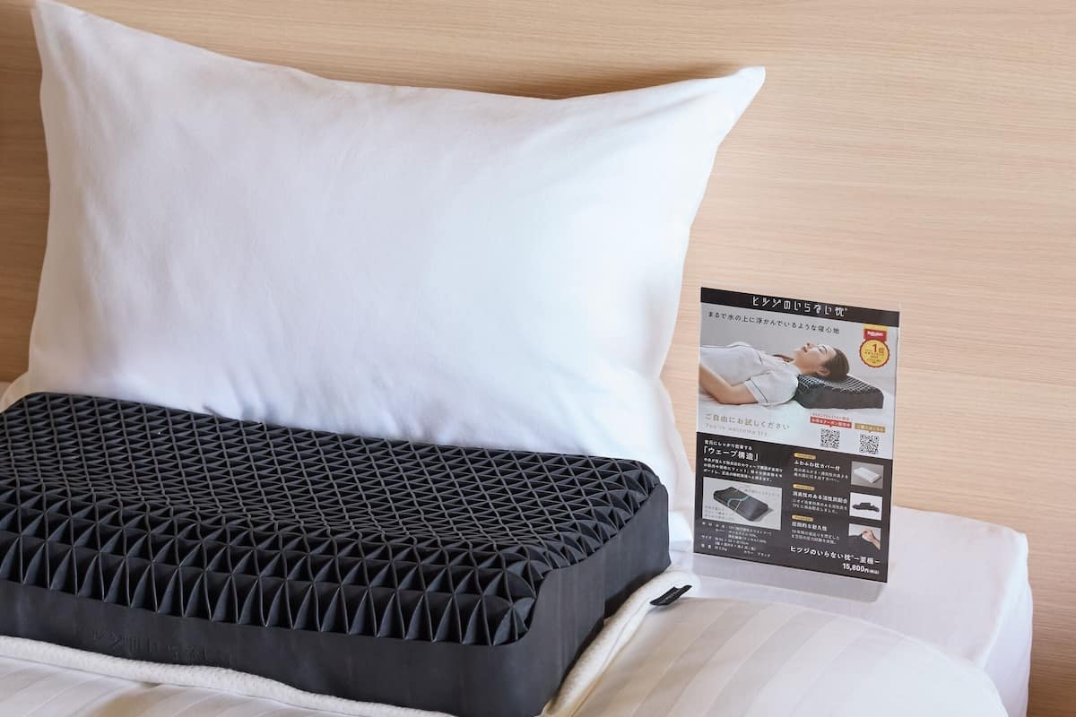 A bed with a white pillow and a black mattress topper.