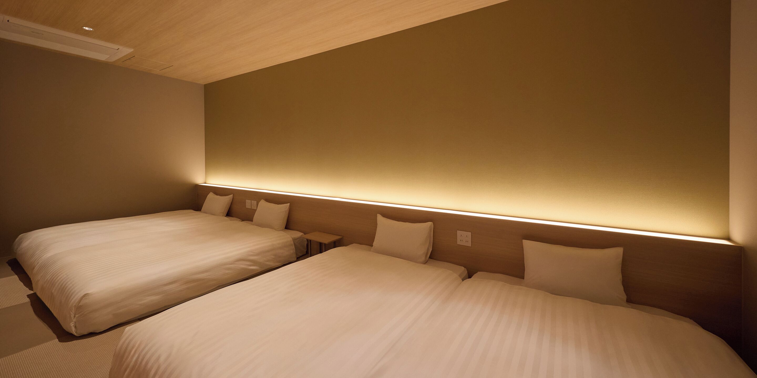 A hotel room with two beds, a wooden ceiling, and a wall-mounted light fixture.