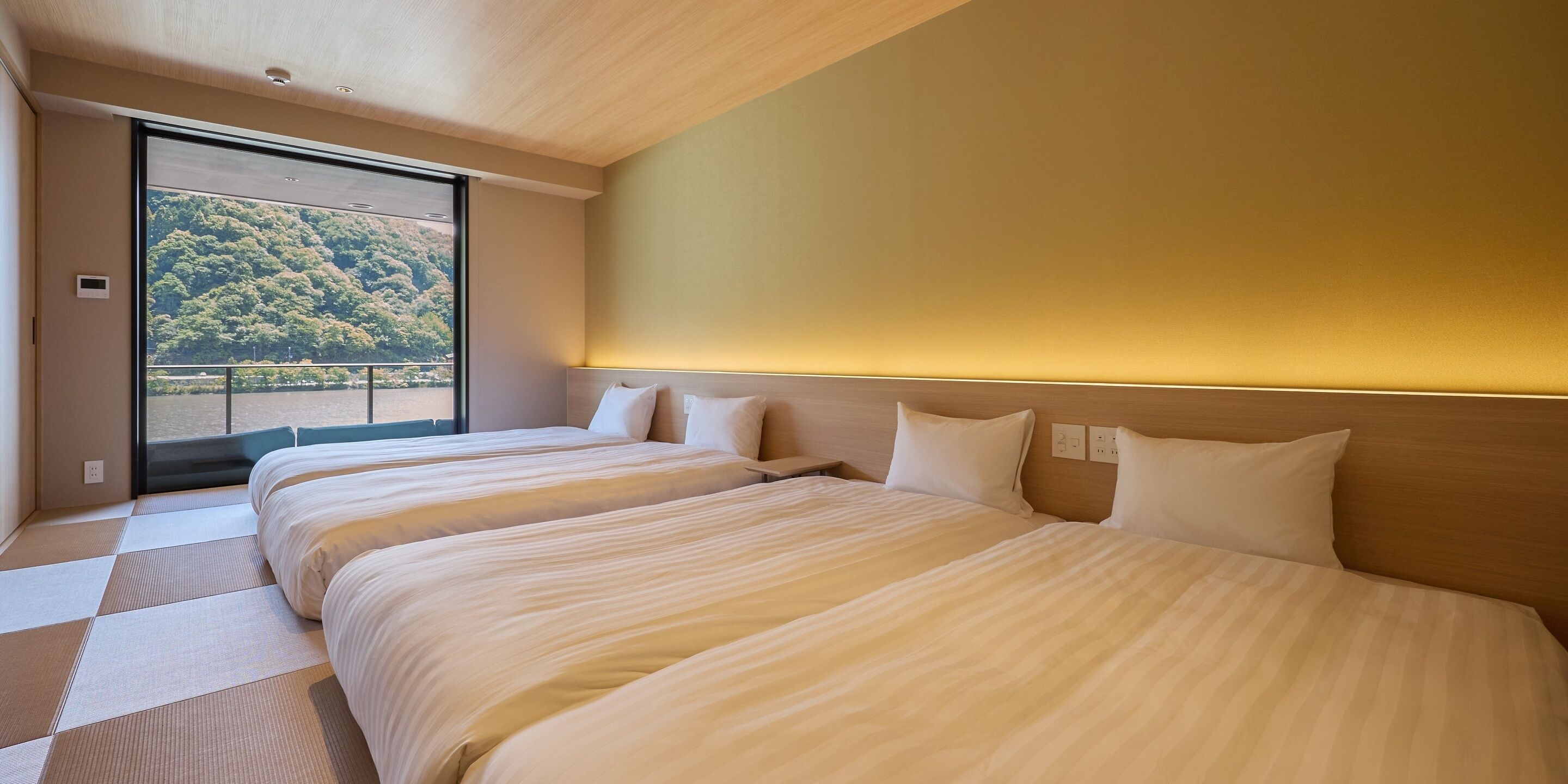 A hotel room with two beds, a large window, and a view of a forested area.