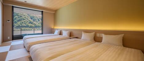 A hotel room with two beds, a large window, and a view of a forested area.
