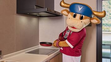 A mascot in a kitchen area with a stove, a sink, and a window with a view.