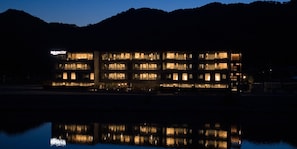 A multi-story hotel with illuminated windows, a reflection in the water, and a sign reading 'Rooftop Stay'.