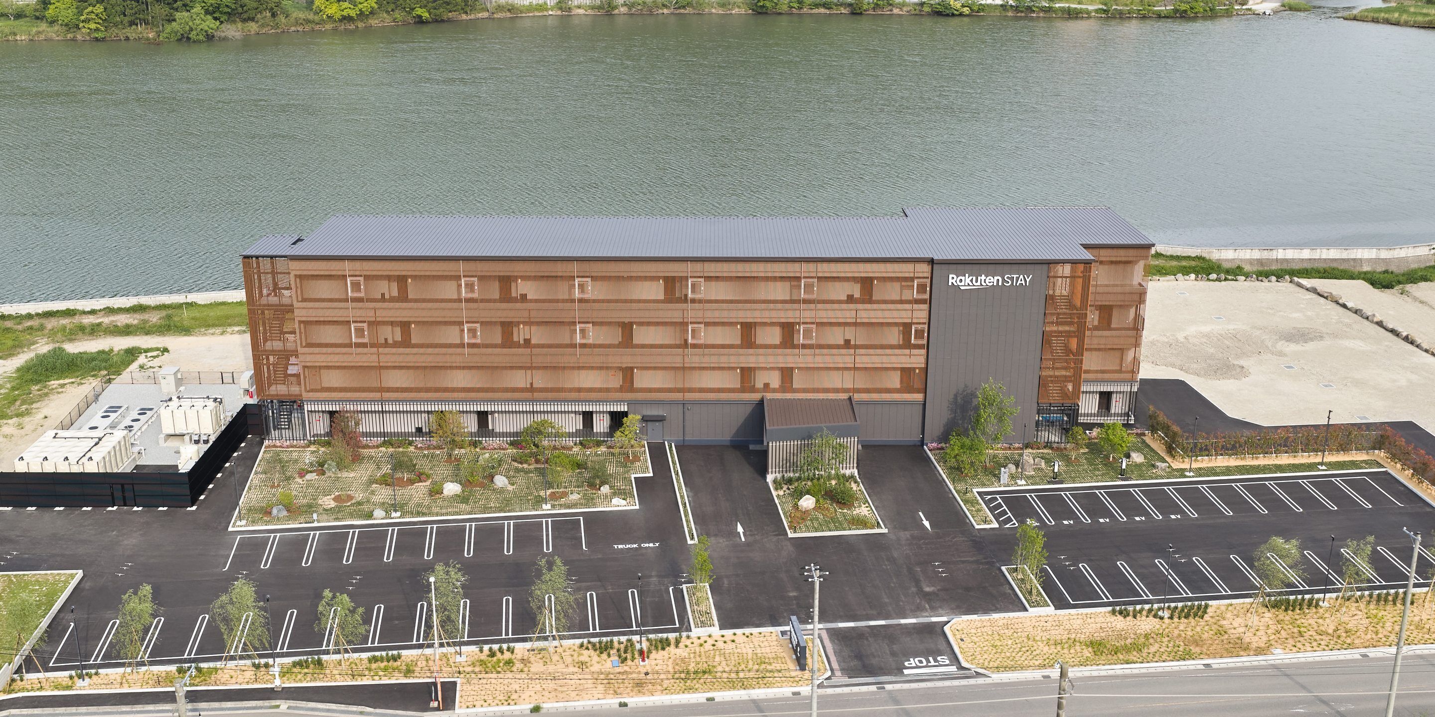 Un edificio con tetto piatto, un parcheggio con posti delimitati e un cartello con scritto 'Rakuten STAY'.