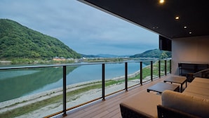 A balcony with a view of a river and hills, furnished with a sofa and a table.