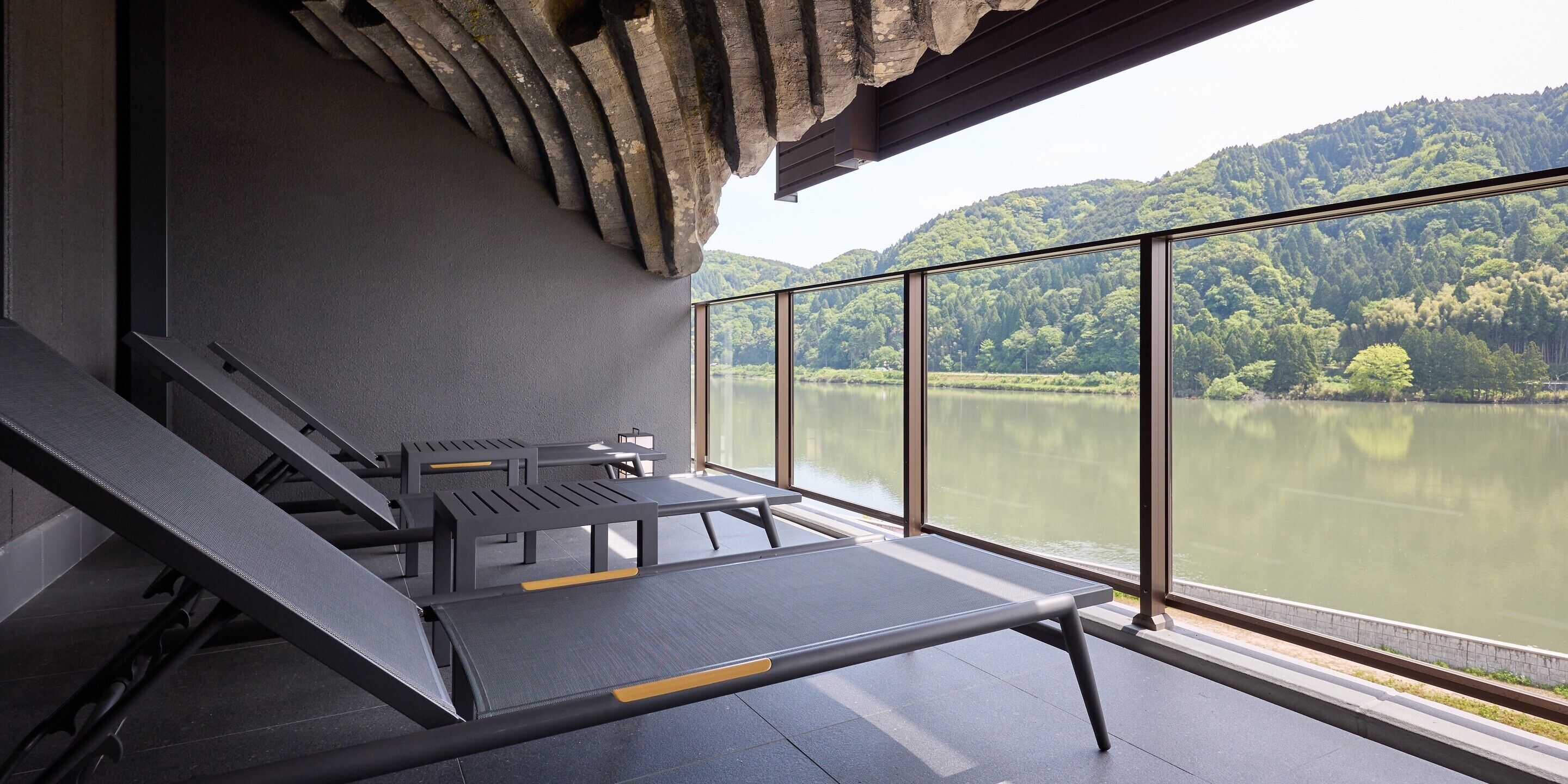 A modern outdoor seating area with a view of a lake and forested hills.