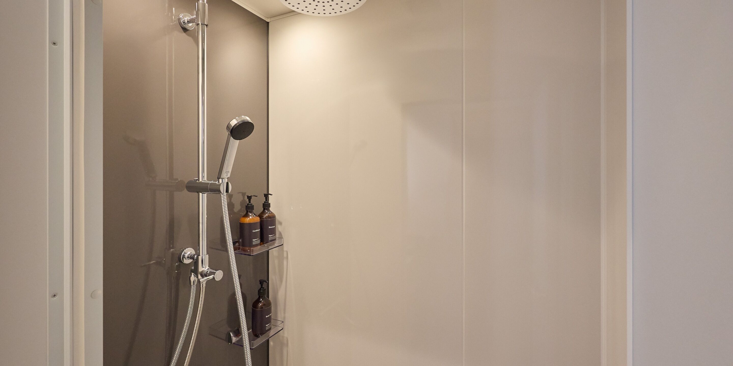 A shower with a handheld showerhead, a wall-mounted faucet, and two shelves with bottles.