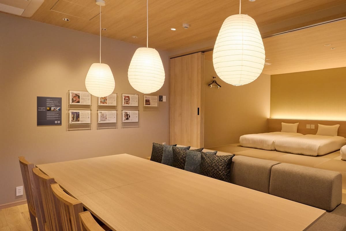 A hotel room with a wooden dining table, two sofas, and hanging paper lanterns.
