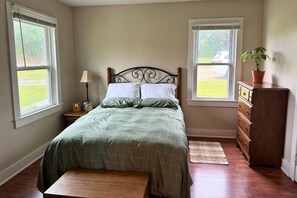 A bedroom with a bed, two windows, a dresser, a lamp, a clock, and a plant. - The Traveler's Cottage - 15 minutes to sports park, downtown and Bourbon Trail (Elizabethtown)