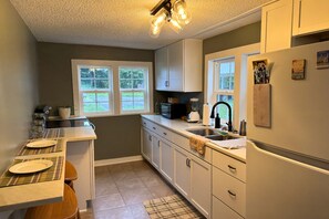A kitchen with a sink, stove, microwave, and cabinets. - The Traveler's Cottage - 15 minutes to sports park, downtown and Bourbon Trail (Elizabethtown)