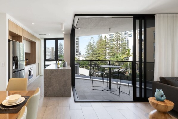 Un apartamento moderno con cocina, comedor y balcón con vistas a edificios y árboles.