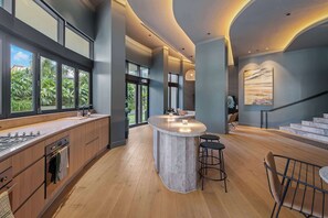 Une cuisine moderne dotée d’un îlot central, de grandes fenêtres et d’un escalier menant à un niveau supérieur.