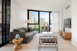 A modern living room with a sofa, a coffee table, a TV, and a view of the city. - 『CASSA VUE』- Cozy Living | Modern 3-BR (Broadbeach)