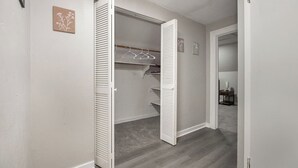 Een inloopkast met witte, vertinde deuren, een houten vloer, en een klein tafeltje met een lamp in de aangrenzende kamer.