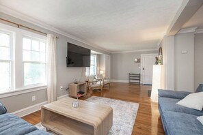 Ein modernes Wohnzimmer mit Flachbildfernseher, einer Couch, einem Couchtisch und einem Sessel.