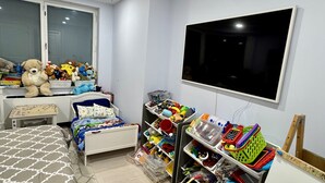 Een kinderkamer met een bed, een bureau, een televisie en planken met speelgoed en opbergmanden.