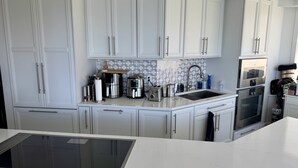 Een moderne keuken met witte kastjes, een inbouwoven, een spoelbak en een koffiezetapparaat.
