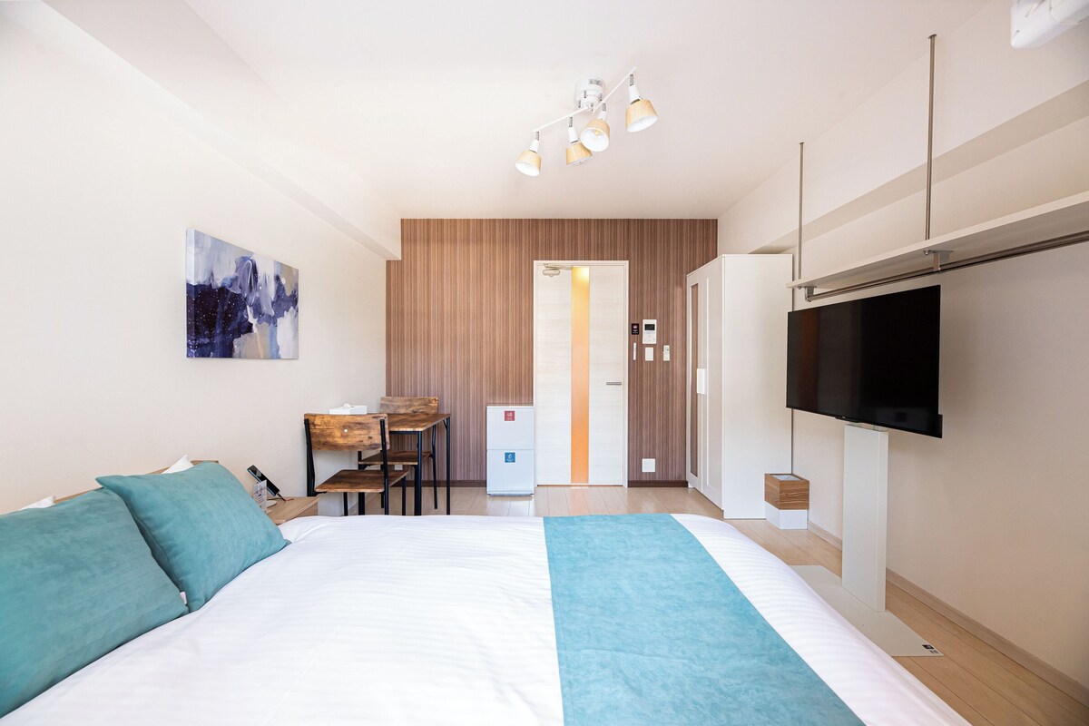 A hotel room with a bed, a desk, a TV, and a painting on the wall.