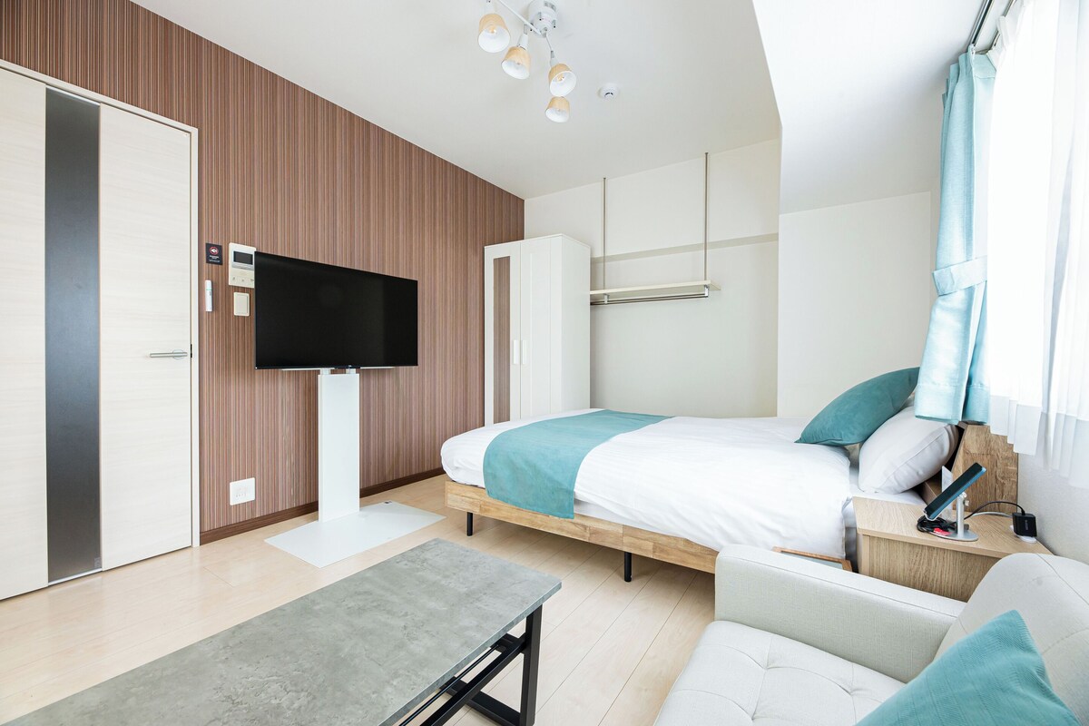 A modern hotel room with a bed, a TV, a desk, and a sofa.