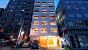 A multi-story building with a central entrance, parking spaces, and a visible sign for 'Uni Brilliant HKT.' - Uni Brilliart Hakata (Fukuoka City)