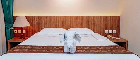 A hotel room with a wooden headboard, a bed with a patterned bedspread, a bedside lamp, a telephone, and a plush toy on the bed.