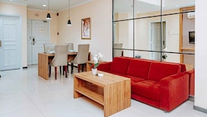 A modern living room with a red sofa, wooden coffee table, and dining area with chairs. - PURI DARMO SERVICED RESIDENCE (Surabaya)