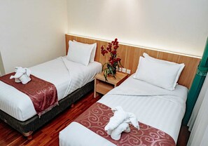 A hotel room with two beds, each with white linens and a red patterned bedspread. There is a wooden nightstand between the beds with a vase of red flowers. - PURI DARMO SERVICED RESIDENCE (Surabaya)