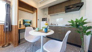 Une cuisine compacte dotée d’appareils électroménagers modernes, un coin repas avec des chaises blanches et une plante en pot.