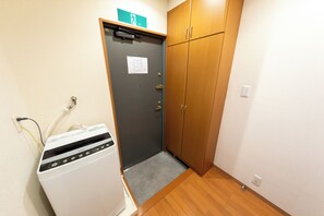 Um quarto com porta cinza, guarda-roupa de madeira e um eletrodoméstico branco à esquerda.