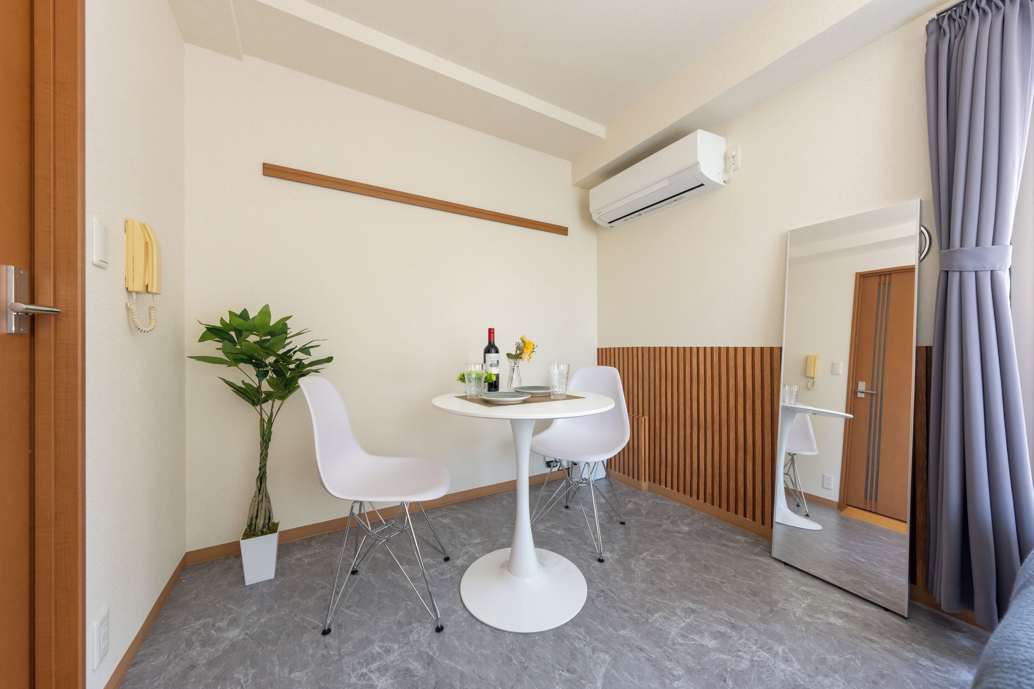 Ein Hotelzimmer mit einem runden weißen Tisch, zwei weißen Stühlen, einem Blumentopf, einem Spiegel und einer Wandpaneele aus Holz.